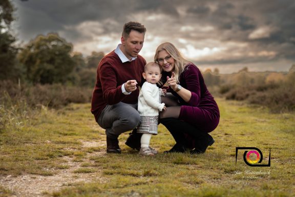 Familie posiert zusammen in der Natur, das Kind in der Mitte, alle lächeln.