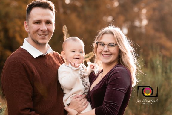 Familie mit einem Baby, glücklich lächelnd in einer herbstlichen Umgebung.