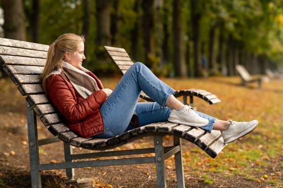 Frau sitzt entspannt auf einer Bank und genießt die herbstliche Landschaft.